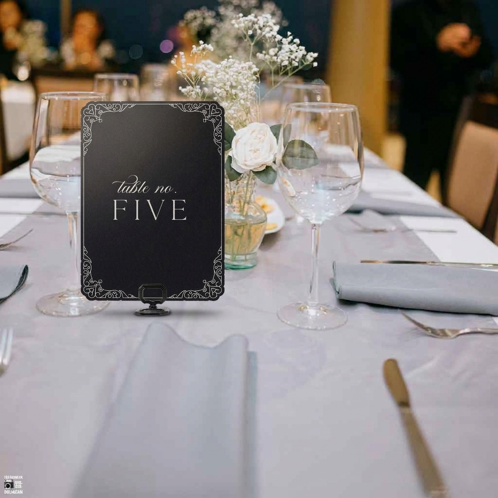 Table setting with a black table number card labeled 'table no. FIVE' on a white tablecloth.
