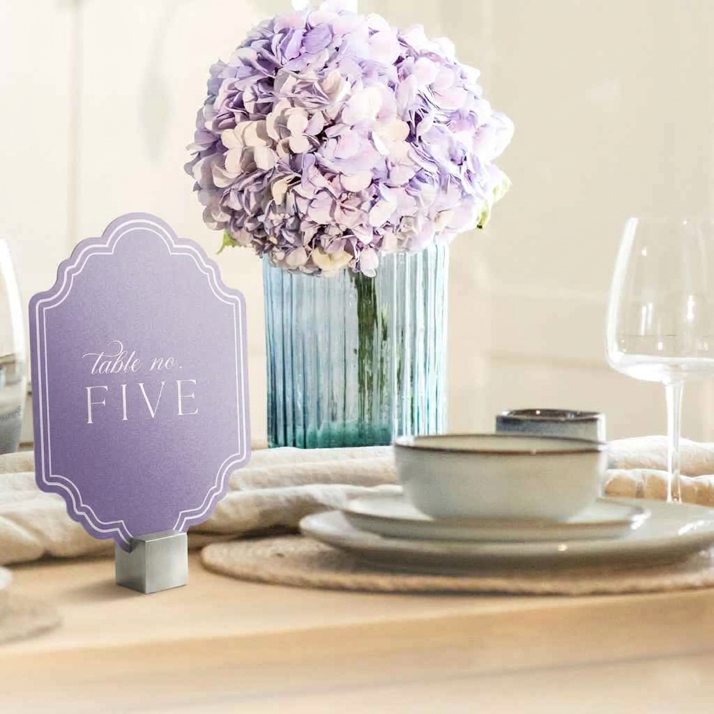 Table setting with a purple wedding table card and floral arrangement on a wooden table.