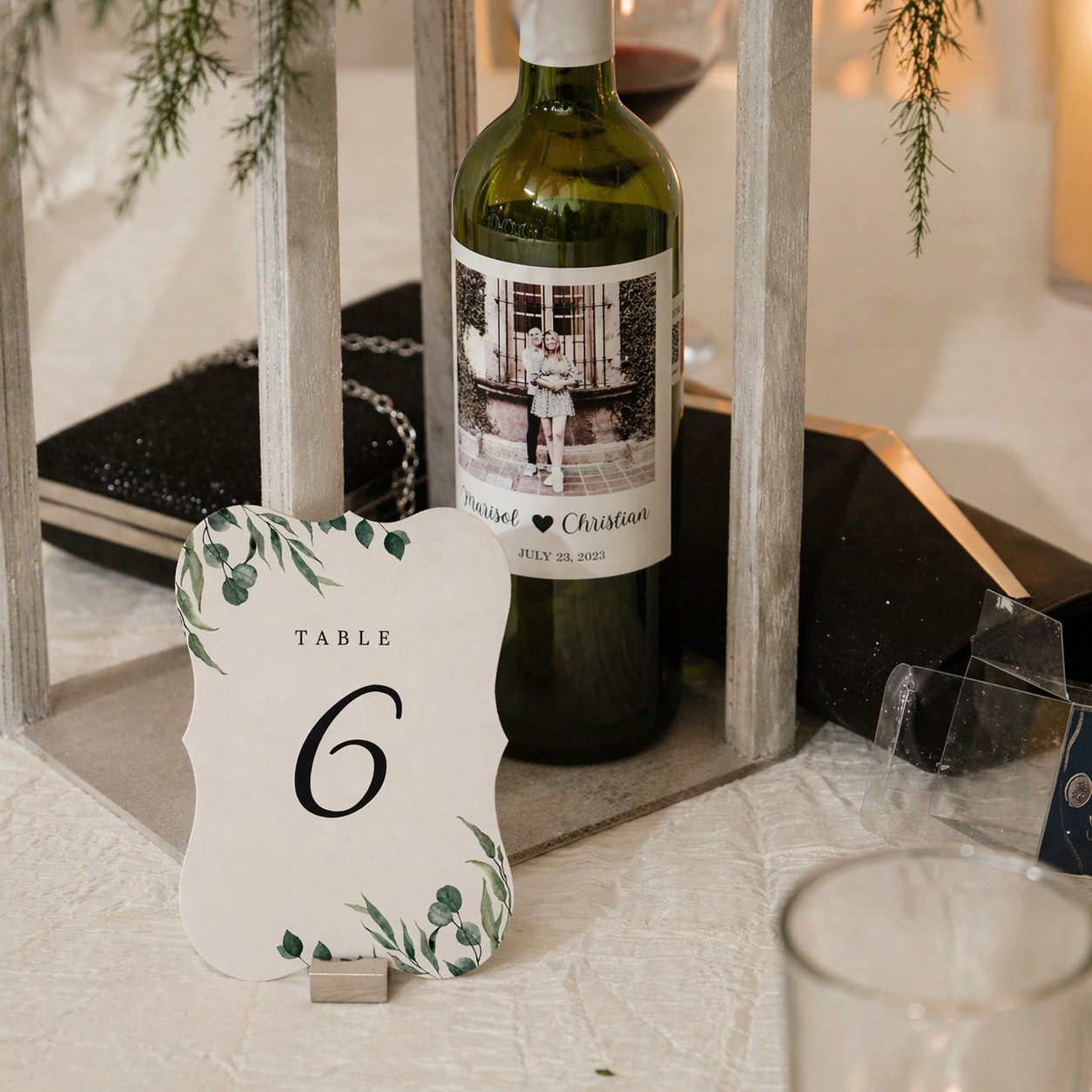 Table number card with decorative elements next to a wine bottle on a table.