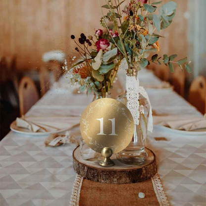 Decorative table setting with a gold wedding table number on a wooden stand, surrounded by flowers and lace.