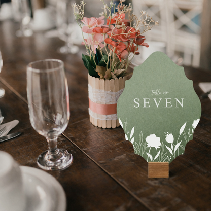 Table setting with a floral centerpiece and a table number sign on a wooden table.