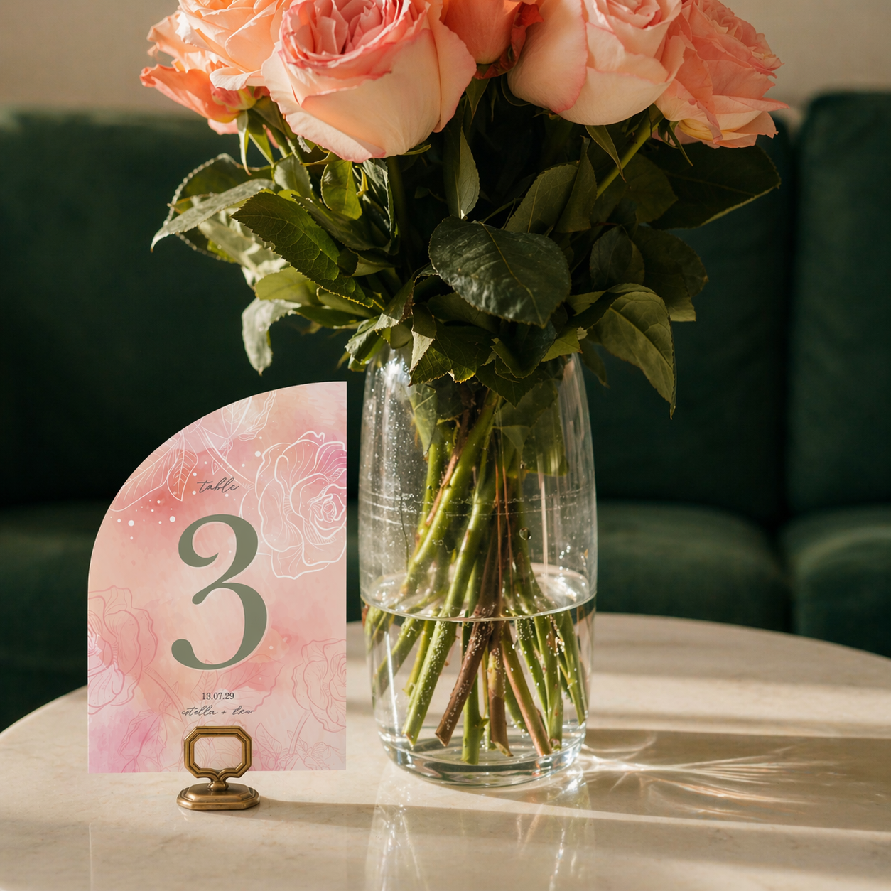 Bouquet of pink roses in a clear vase with a table number card on a marble surface.