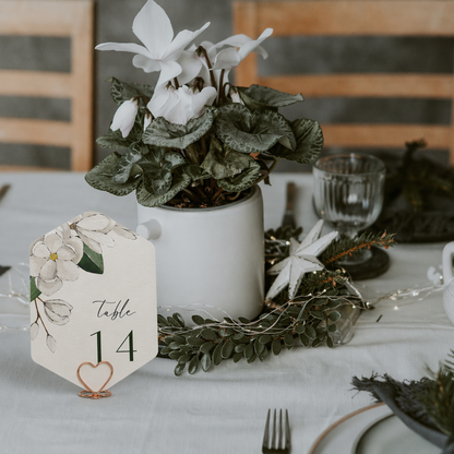 Decorative table setting with a plant, wedding table number card, and floral decorations on a table.