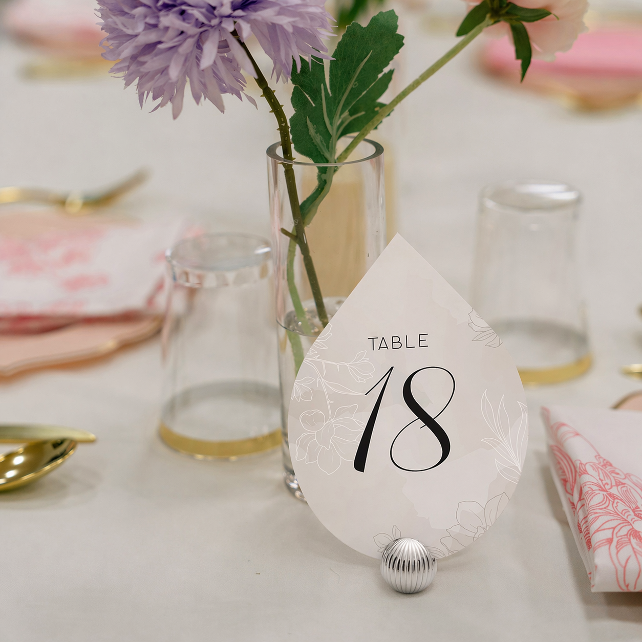 Teardrop-shaped table number card on a decorative table setting with flowers and glasses.