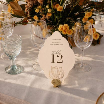 Decorative table setting with flowers, glasses, and a table number card on a white tablecloth.