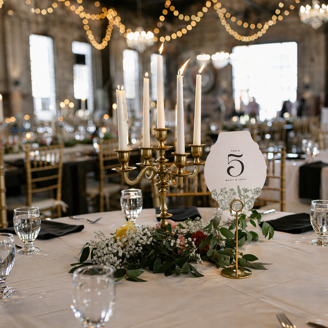 Decorative table setting with candles, flowers, and a table number in a banquet hall.