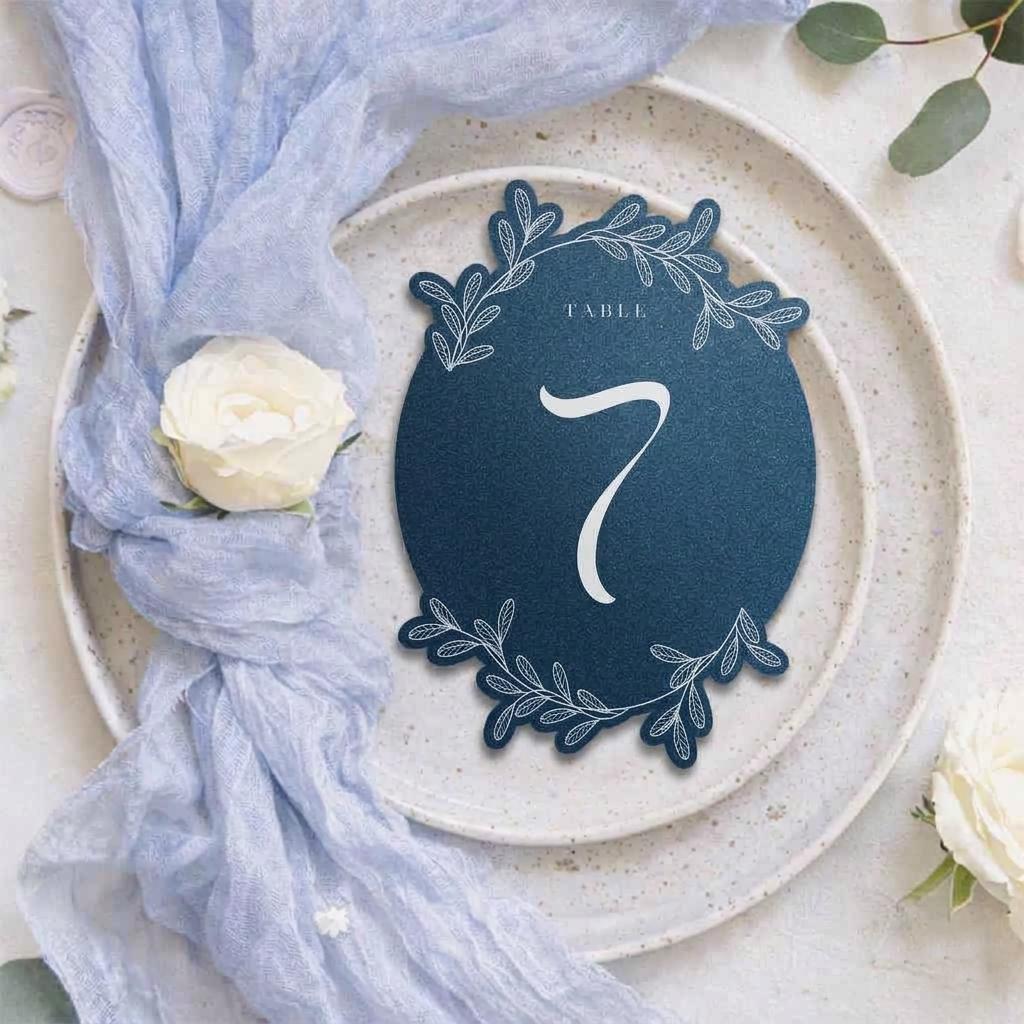 Navy blue table number card with decorative elements on a white plate with a white rose.