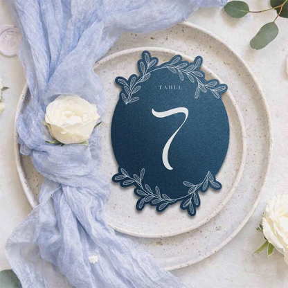 Navy blue table number card with decorative elements on a white plate with a white rose.