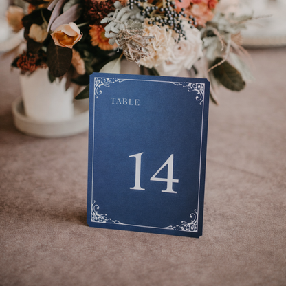 Navy blue table number card with '14' on a textured surface with flowers in the background