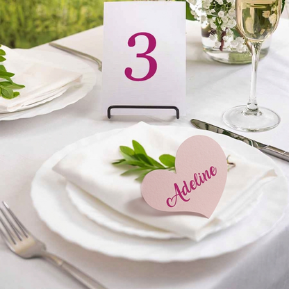 Table setting with a pink heart-shaped name card and table number 3 on a white tablecloth.