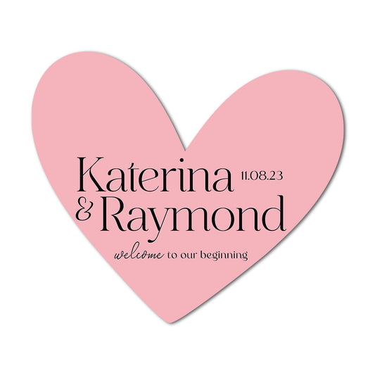 Pink heart-shaped favor card with names 'Katerina & Raymond' and date '11.08.23' on a white background