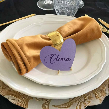 Napkin folded on a plate with a purple heart-shaped name tag labeled 'Olivia' on a decorative table setting.