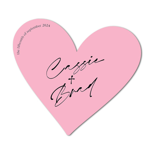 Pink heart-shaped favour card with 'Cassie & Brad' and a date on a white background